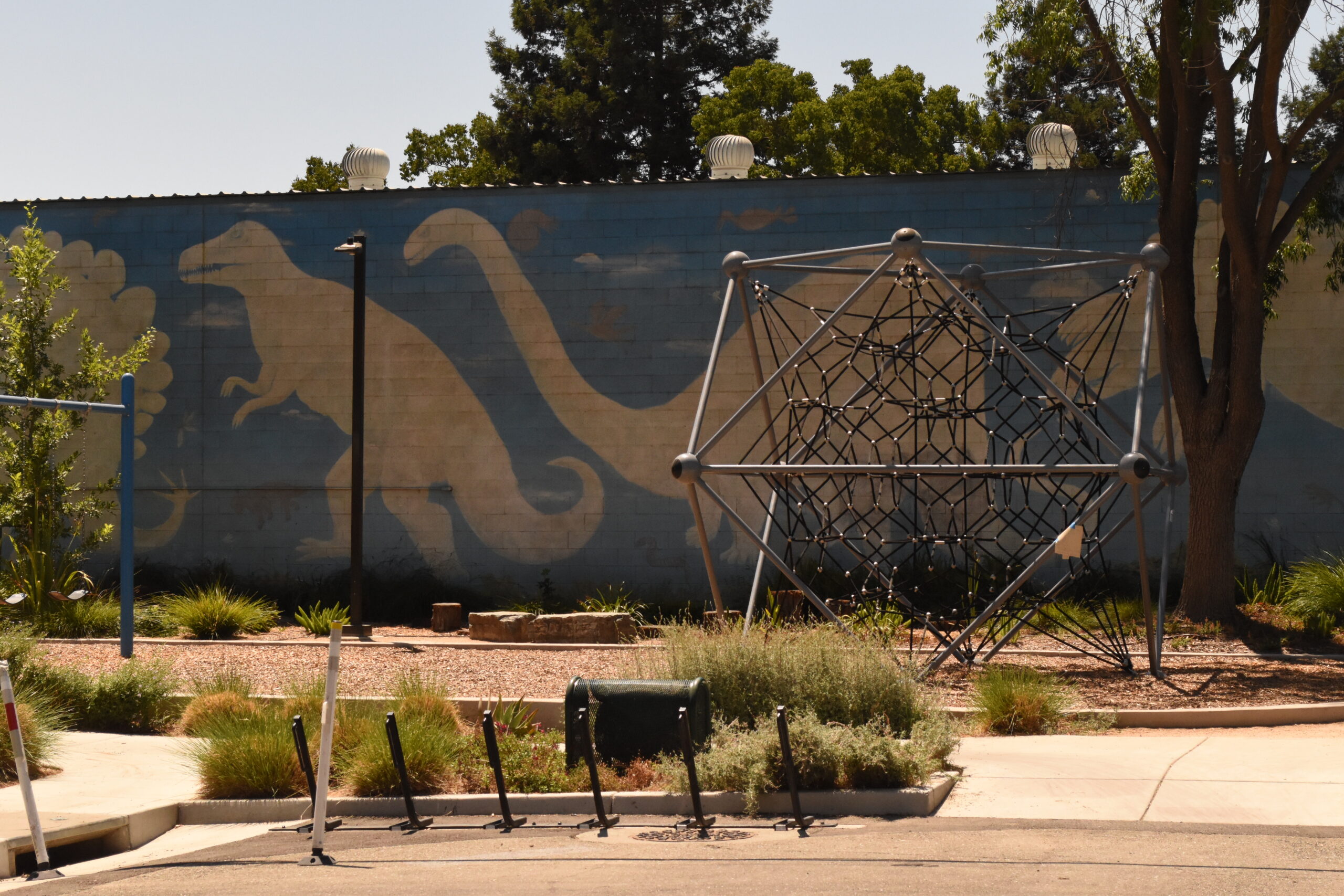 Play structure at a park with a dinosaur mural in the back.