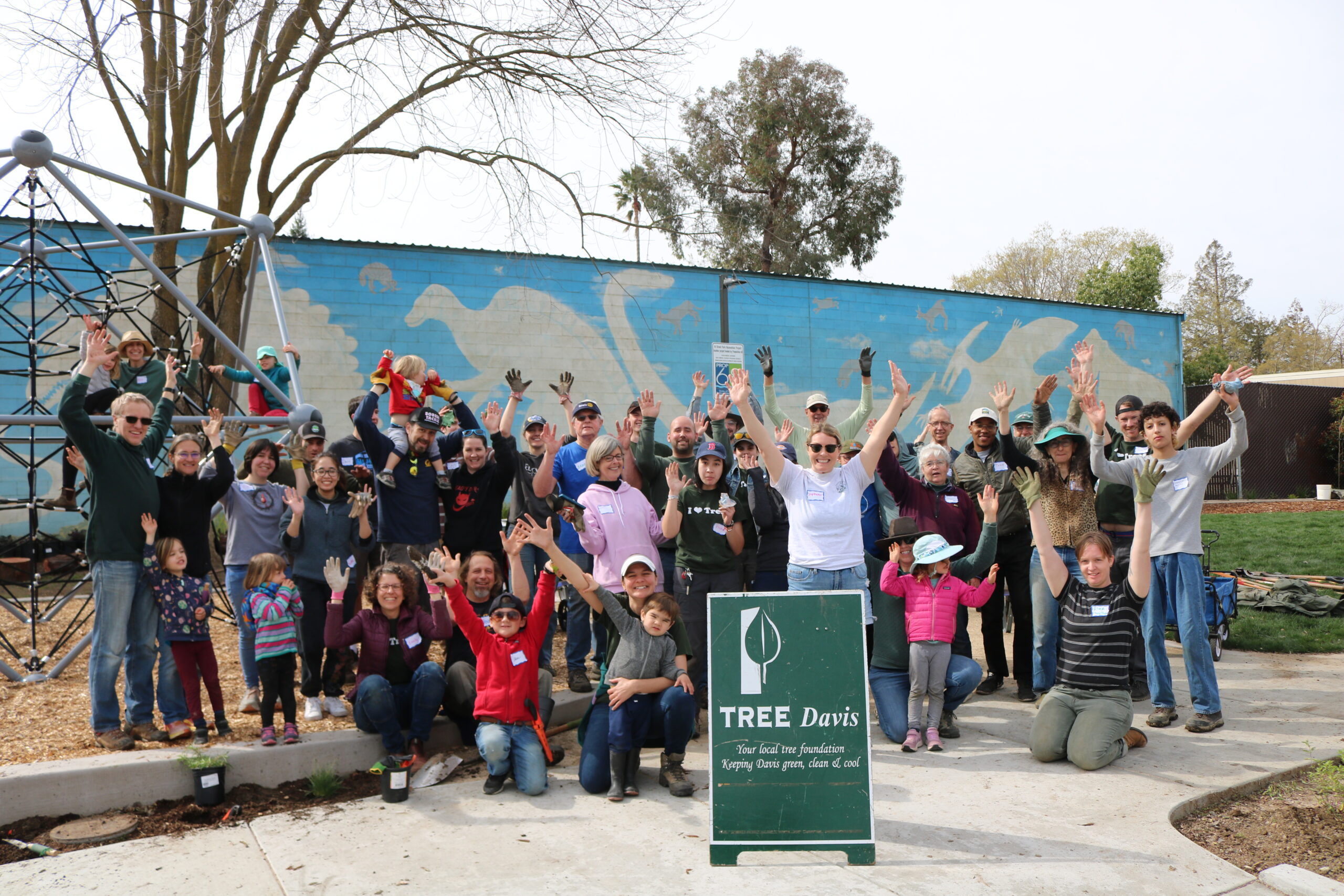 A large group of volunteers smile and pose with a Tree Davis sign.