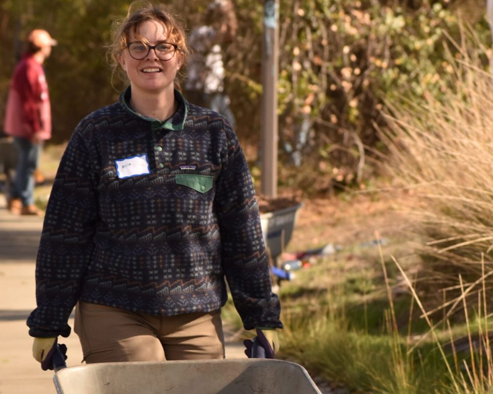 Tree Davis intern smiles and pushes wheelbarrow.