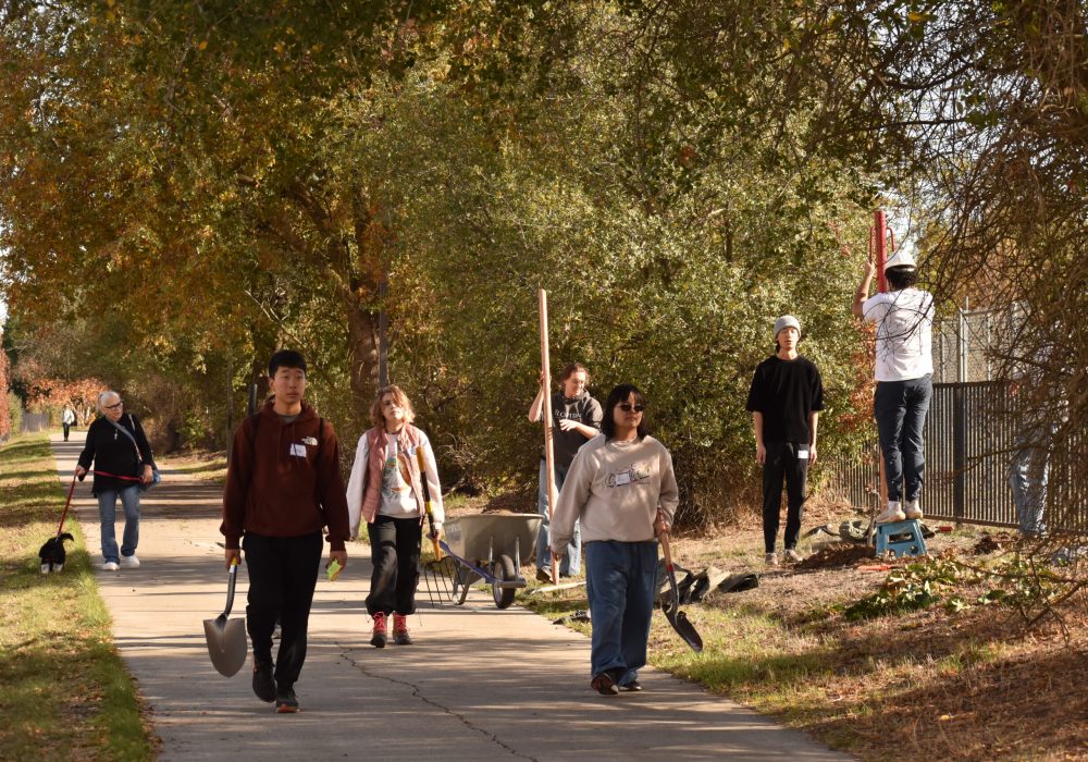 Volunteers carry tools and others plant trees in the background.