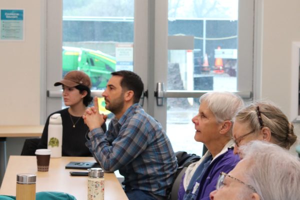 Green Volunteers sit at table and listen to lecture.